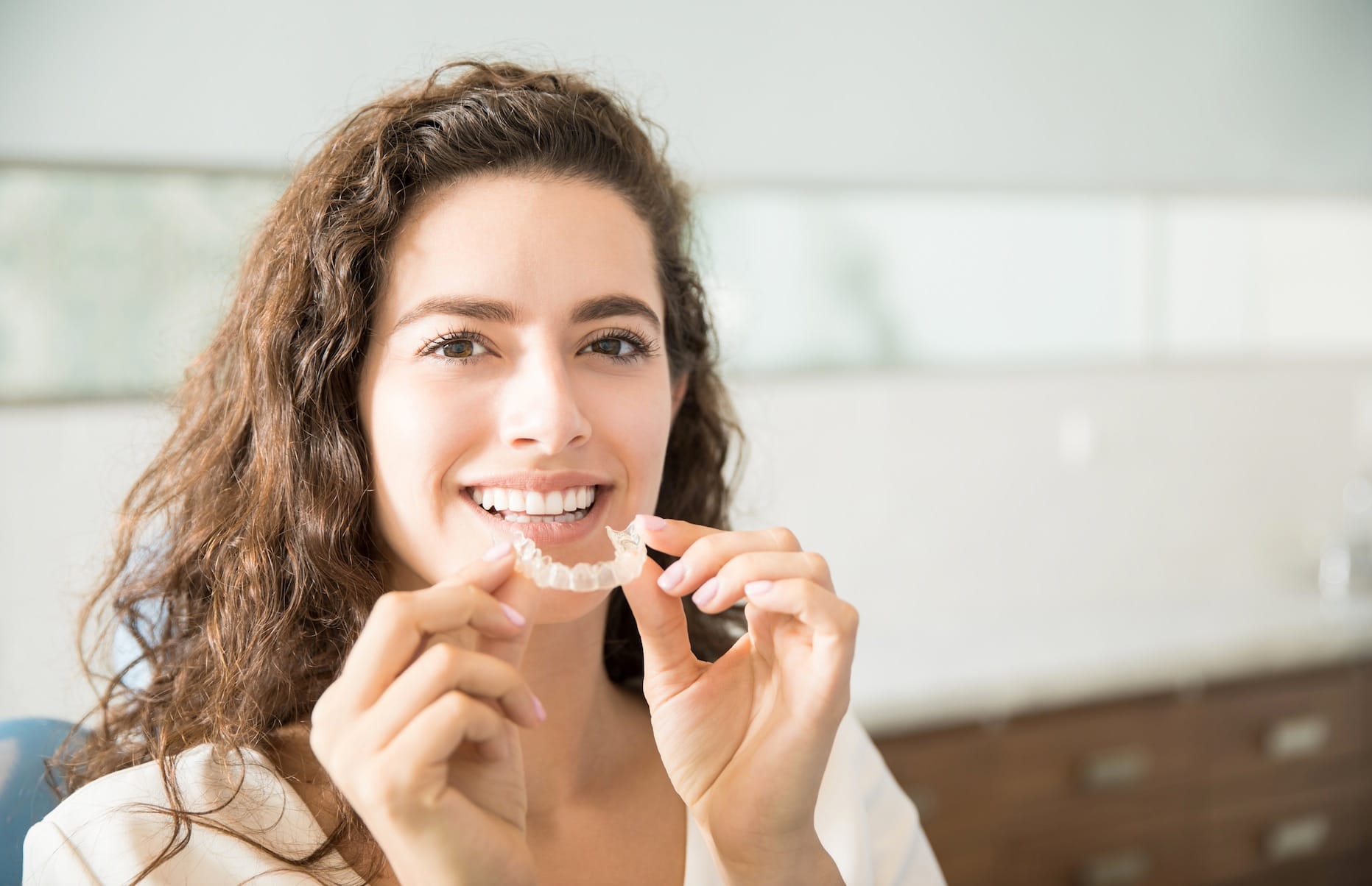 Woman smiling, holding clear aligners Woman smiling, holding clear aligners
